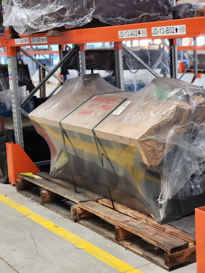 engine block wrapped in plastic, on timber pallet in workshop.