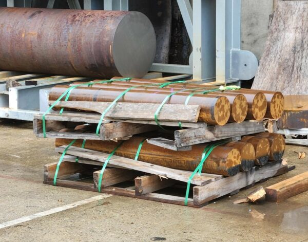 Cylindrical components in a yard, stored on stacked, broken timber pallets - showing signs of damage